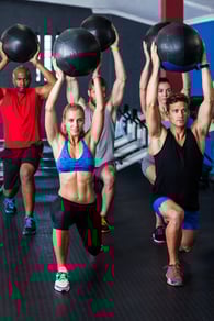 Friends holding fitness ball while exercising in gym